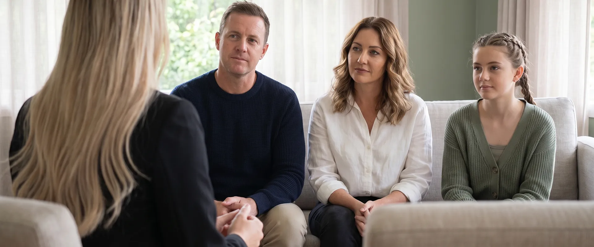 A Target Behaviour Services practitioner sits across from a father, mother and teenage daughter on a couch during an interim behaviour support discussion.