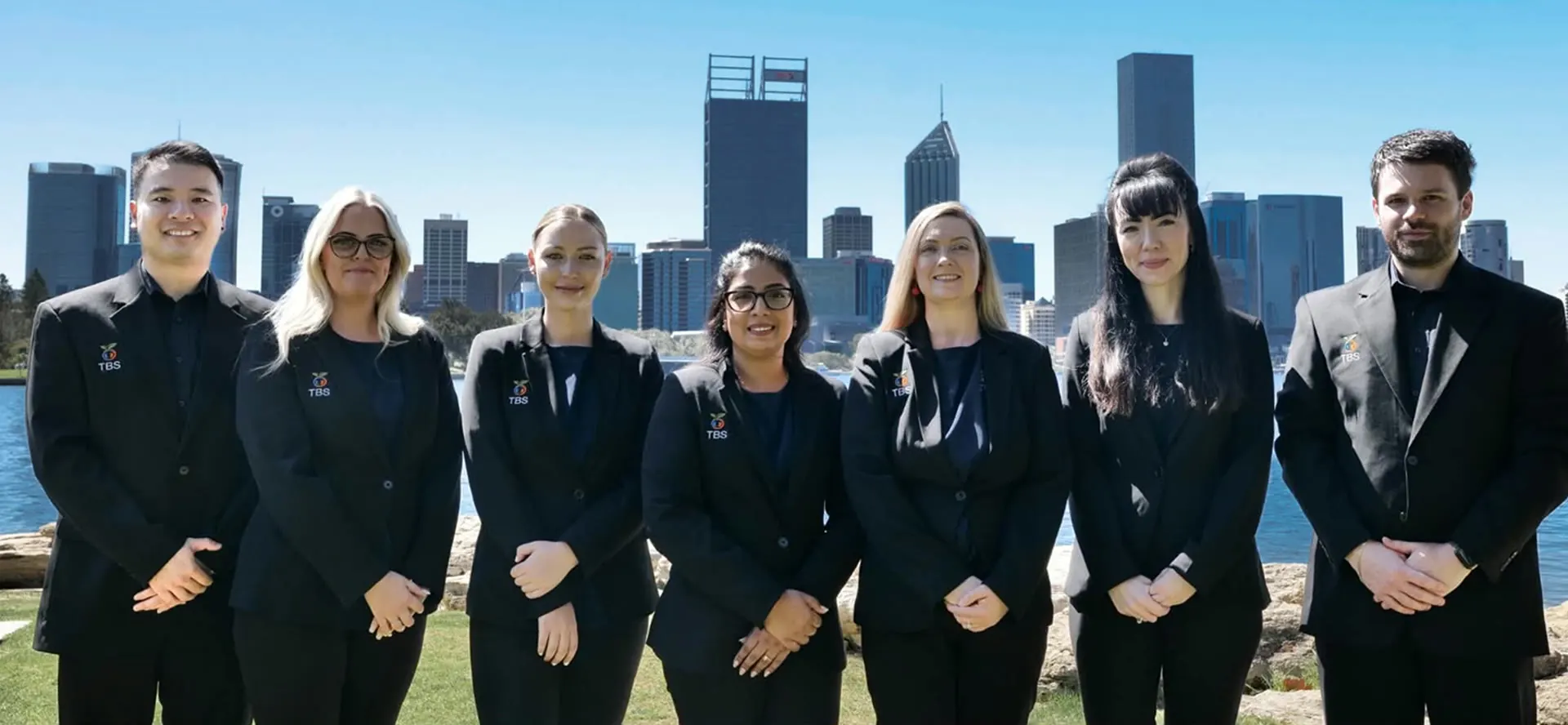 The Target Behaviour Services team standing together by the Perth riverfront with the city skyline behind them.